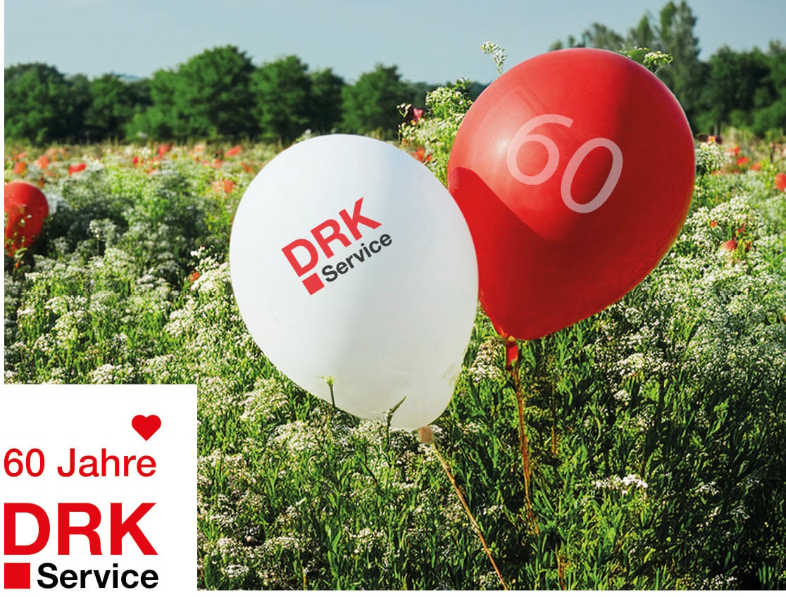 Ein roter und ein weißer Ballon mit DRK-Service Logo und der Zahl 60 auf einer Wiese