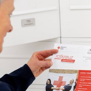 Imagebild Mitgliederkommunikation. Eine Frau steht vor ihrem Briefkasten und hält einen Brief vom Roten Kreuz in ihren Händen