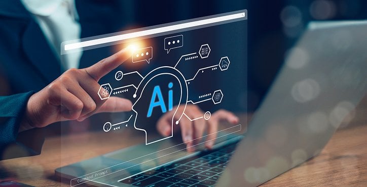 Finger einer Person zeigt auf ein AI-Hologramm vor einem Laptop. Die Fingerkuppe leuchtet.