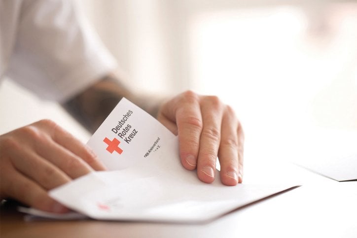 Nahansicht einer Person, die gerade einen Briefbogen mit DRK-Logo faltet.
