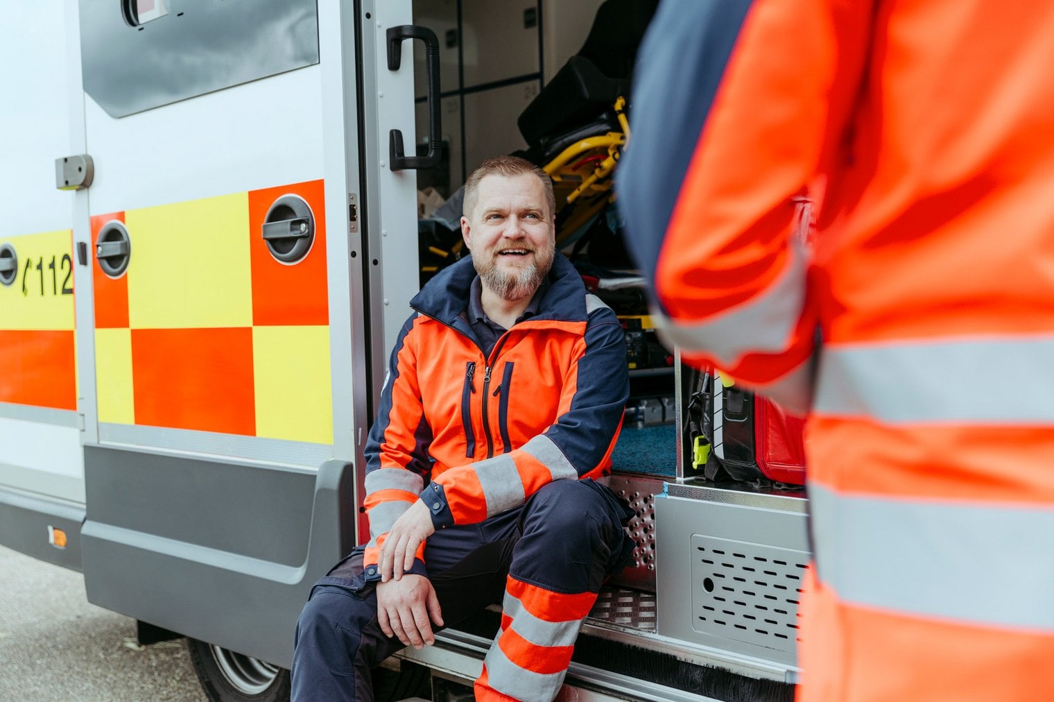 Ein Rettungssanitäter sitzt auf der Stufe eines Rettungswagens und schaut einen anderen Sanitäter an, der vor ihm steht